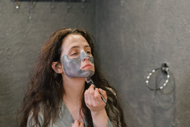 A woman applies a facial mask as part of her skincare routine in a modern bathroom.